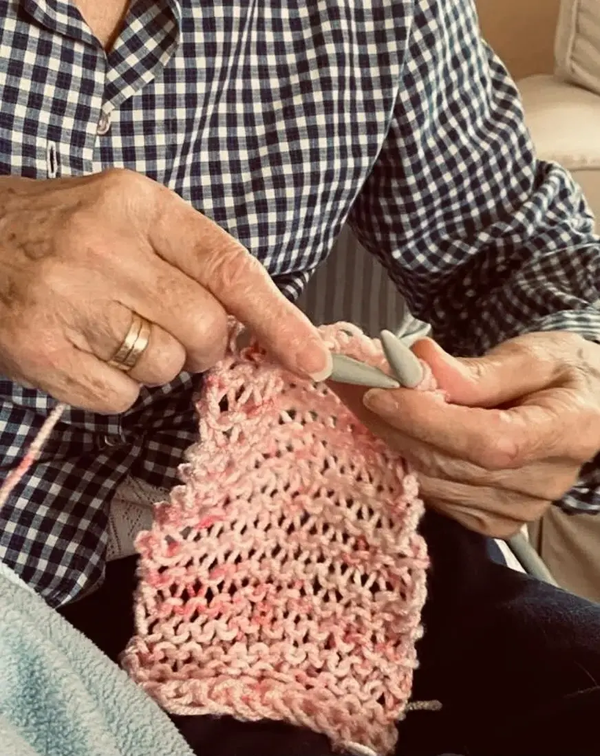 Le mani di nonna Giusy al lavoro con un filato rosa
